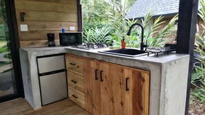 A kitchen with a built-in sink, wooden cabinets, a coffee maker, and a microwave. - Cabañas Naturaleza (Bocas del Toro)