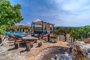 A stone pool area with lounge chairs, a pergola, and a view of the countryside.