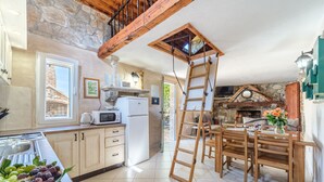 Une cuisine avec des murs en pierre, des poutres en bois, un réfrigérateur blanc, une table en bois avec des chaises et une échelle.
