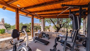 Une salle de sport extérieure abritée, équipée de divers appareils, notamment un vélo elliptique, un tapis de course et des appareils de musculation.