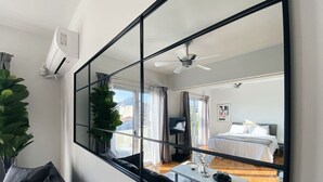 Habitación de hotel moderna con un espejo grande que refleja el dormitorio, un ventilador de techo y vistas a la ciudad.