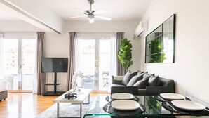 Una sala de estar moderna con una mesa de comedor de vidrio, sofá gris y televisor de pantalla plana.