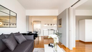 Una sala de estar moderna con un sofá gris, una mesa de centro con un jarrón de flores y una cocina al fondo.