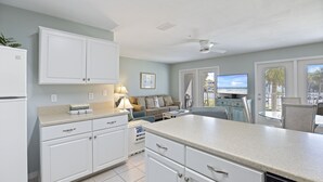 Une cuisine moderne avec des armoires blanches, un grand îlot central et une vue sur la plage par la fenêtre.
