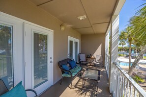 A covered balcony with a wicker chair, a small table, and a pool in the background.