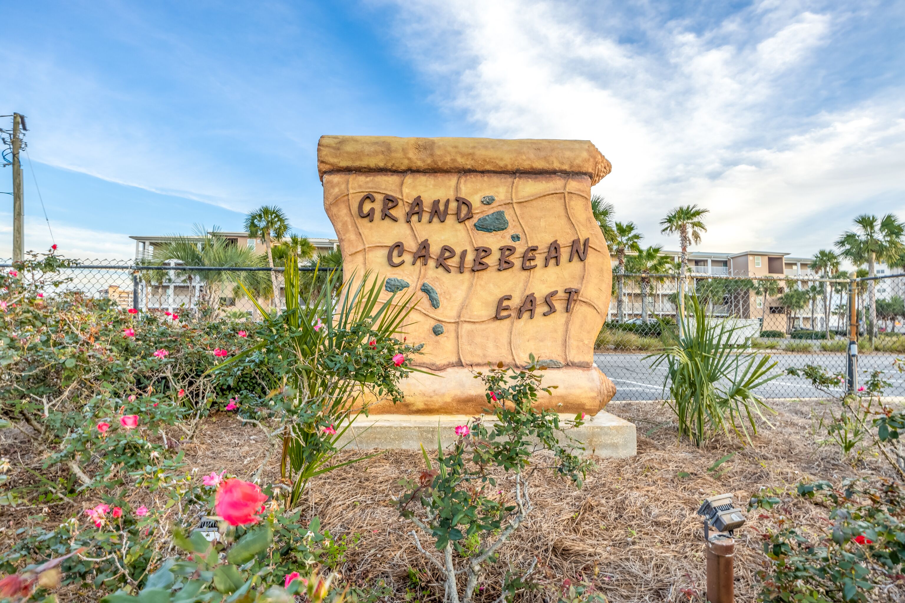 Un grand panneau en pierre portant l’inscription « Grand Caribbean East », entouré de plantes en fleurs et d’une clôture.