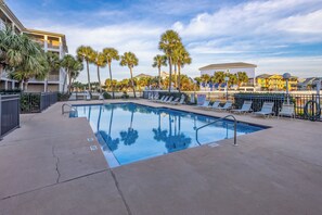A swimming pool with lounge chairs, palm trees, and a building in the background.
