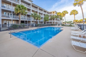 A swimming pool with lounge chairs, palm trees, and a multi-story building with balconies.