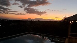 A clear sky with clouds at dusk, a swimming pool, and a distant mountain range.