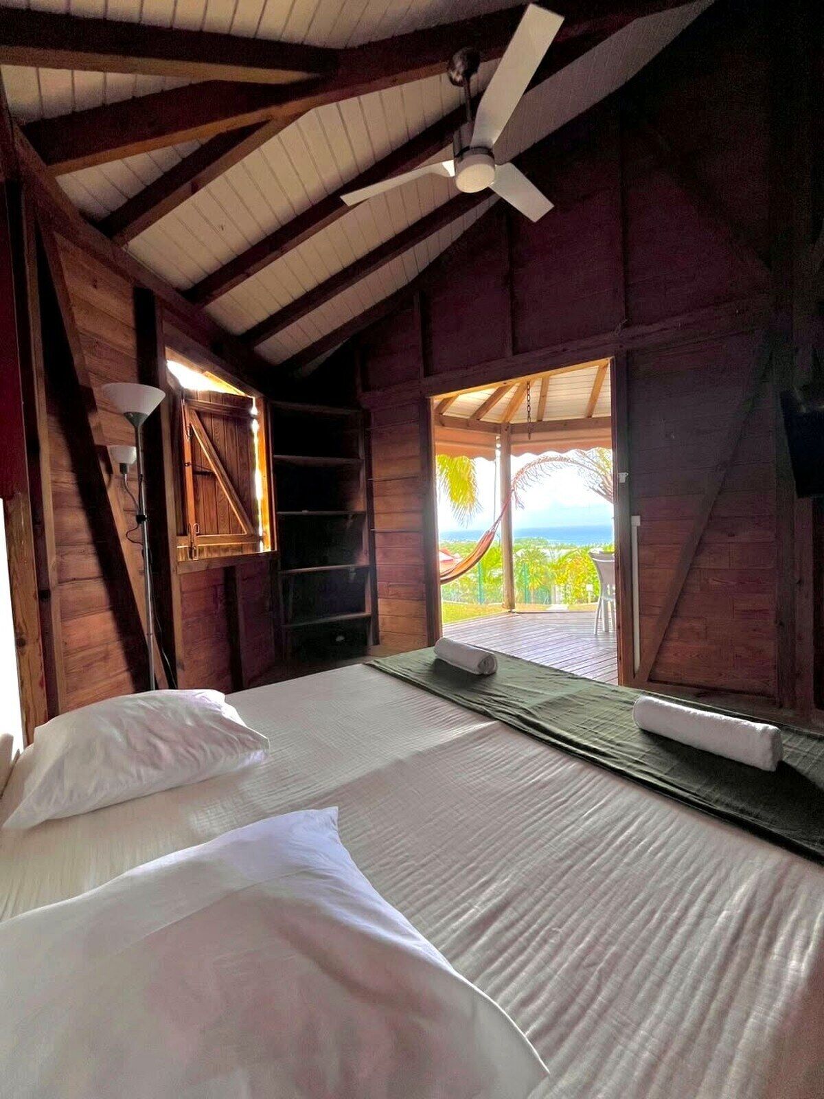 Une chambre avec un lit, un ventilateur de plafond et une vue sur l’extérieur.