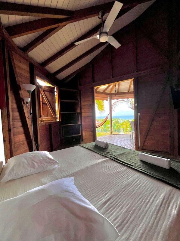 A room with a bed, a ceiling fan, and a view of the outdoors.