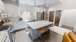 A modern kitchen with white cabinets, a marble island, and bar stools.