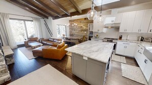 A modern kitchen with white cabinets, a marble countertop, and a dining area with a sofa and table.