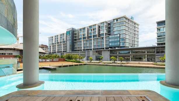A modern hotel with a pool area, featuring a wooden deck and a view of the building's exterior.