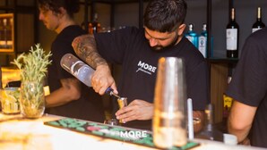 A bartender preparing a drink at a bar with shelves of bottles in the background. - More Ipanema (Rio de Janeiro)