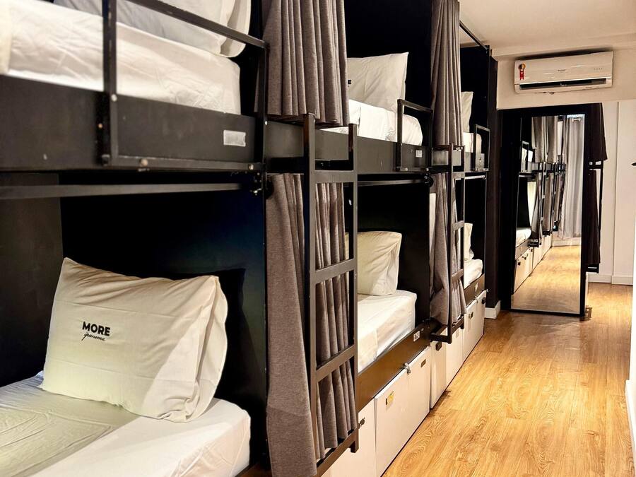 Een rij stapelbedden met opbergladen, een houten vloer en een airconditioning op de muur.