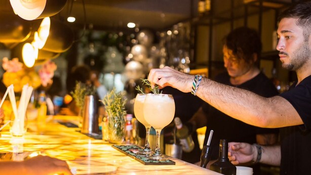 A bar setting with a bartender preparing a drink, a bar counter, and various bar tools. - More Ipanema (Rio de Janeiro)