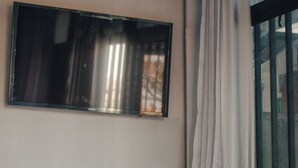 A room with a flat-screen TV mounted on the wall, a window with a curtain, and a small table with a black object on it. - More Ipanema (Rio de Janeiro)