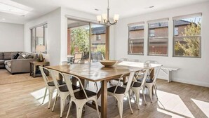 Un'ampia sala da pranzo con un tavolo in legno e sedie bianche, ampie finestre e vista sull'esterno.