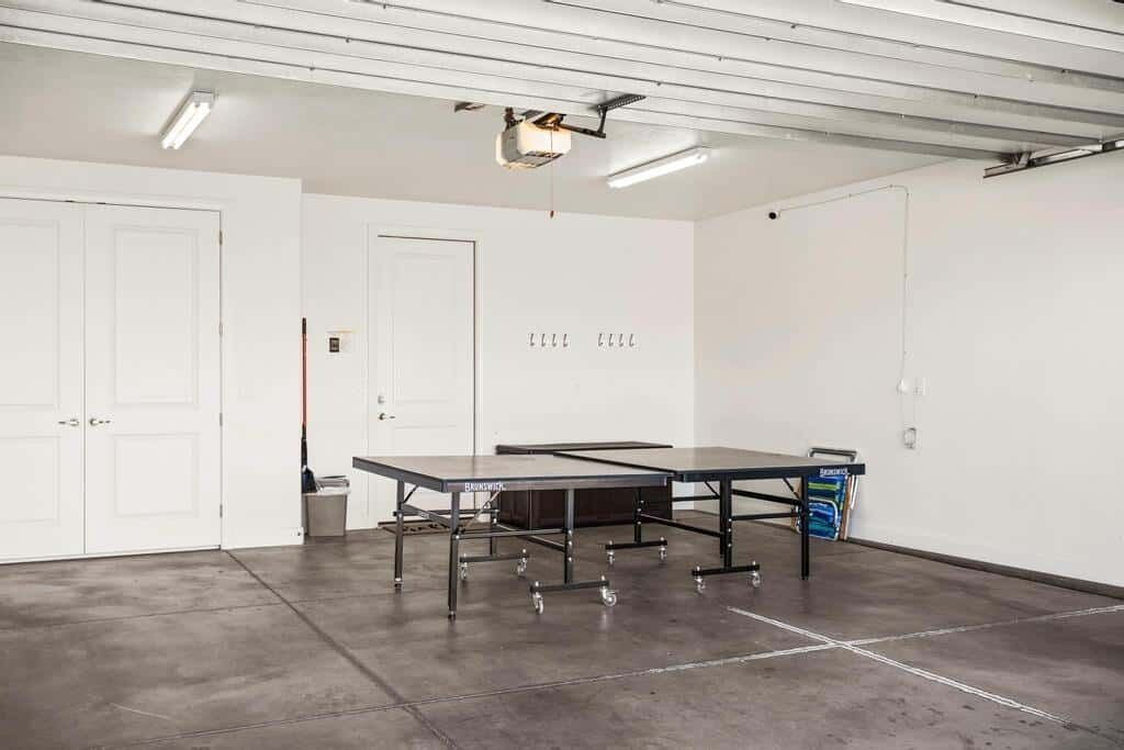 A spacious room with a large table, white doors, and a ceiling-mounted projector.