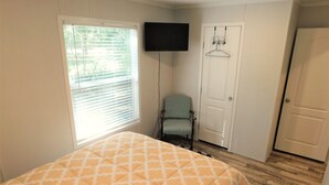Un dormitorio con cama, una silla, televisor y puerta.