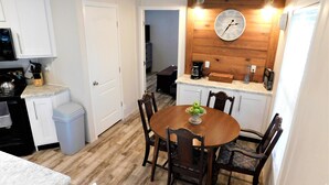 Una cocina compacta con armarios blancos, una mesa de comedor de madera y un reloj en la pared.