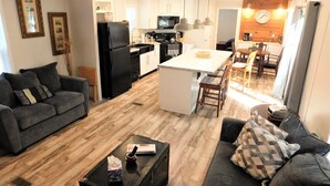 Una sala de estar moderna con un sofá gris, una mesa de centro y una zona de comedor con sillas de madera.