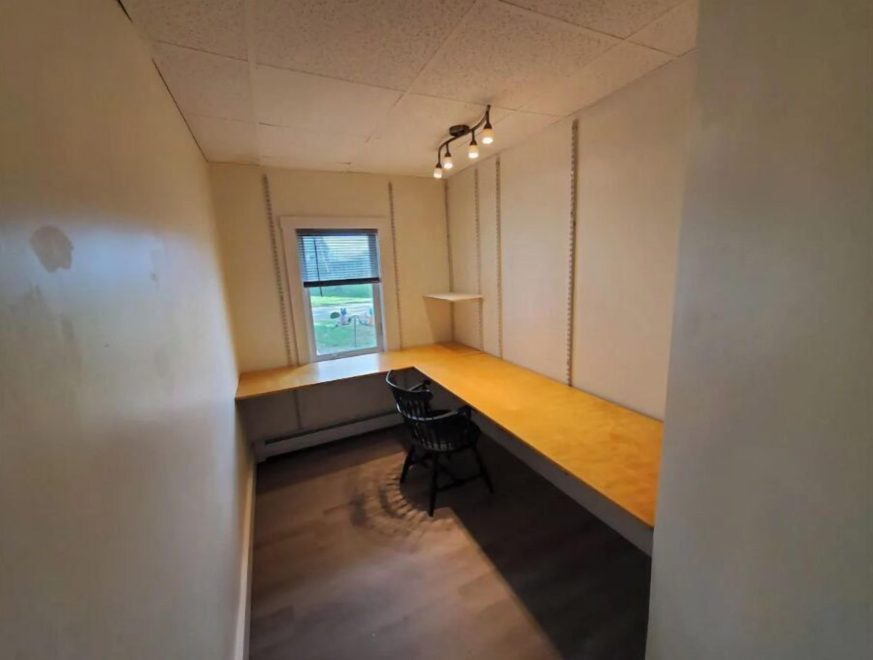 Ein kleiner, schmaler Raum mit einer hölzernen Bank, einem einzelnen Stuhl und einem Fenster.