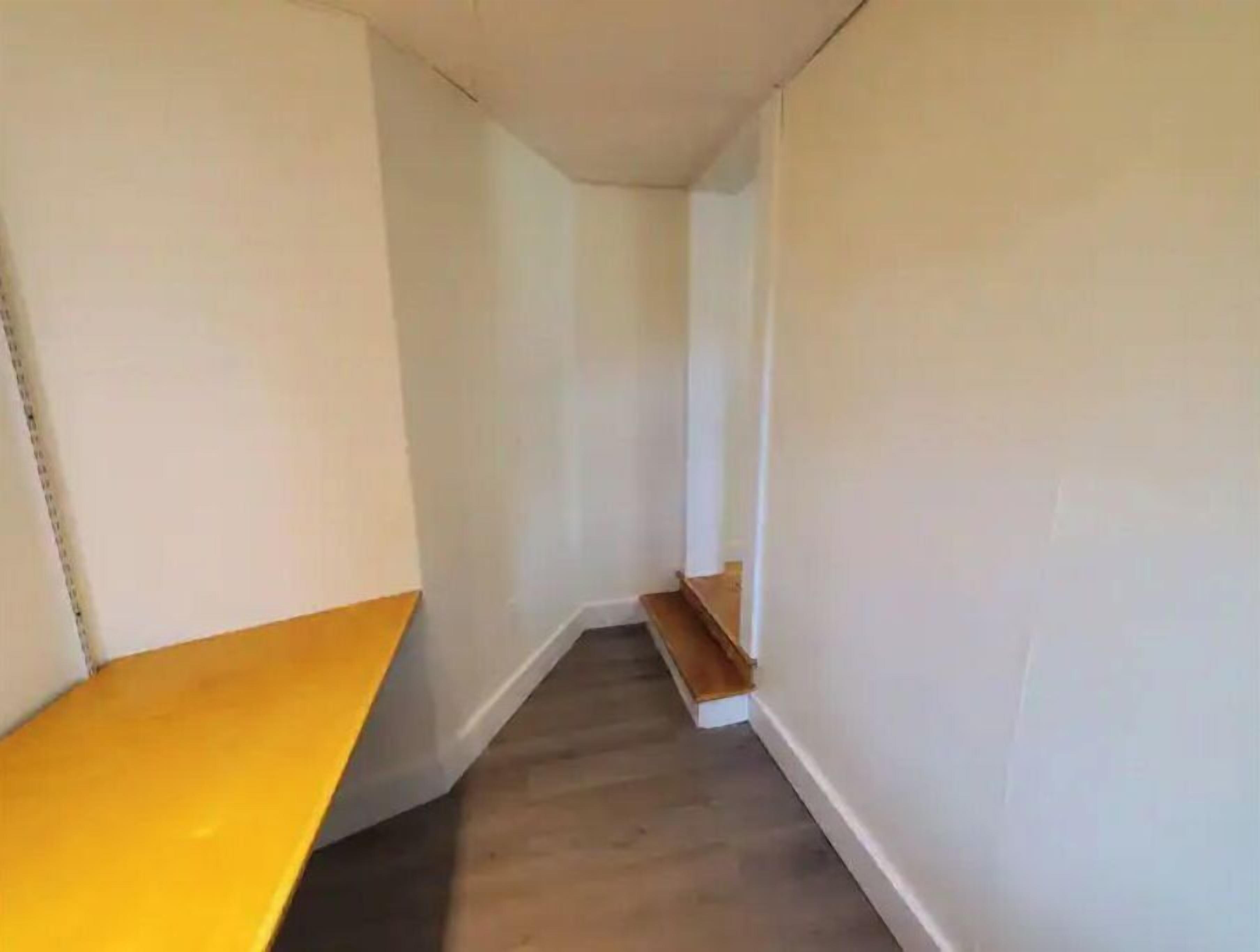 Ein schmaler Gang mit einer Holzbänkl in der linken Wand und einer Holztreppe zur rechten.