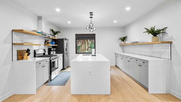 Une cuisine moderne avec des meubles blancs, un îlot central et des étagères en bois.