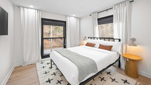 Une chambre à coucher moderne avec un lit, des rideaux blancs, une fenêtre, une lampe de chevet et un tapis.