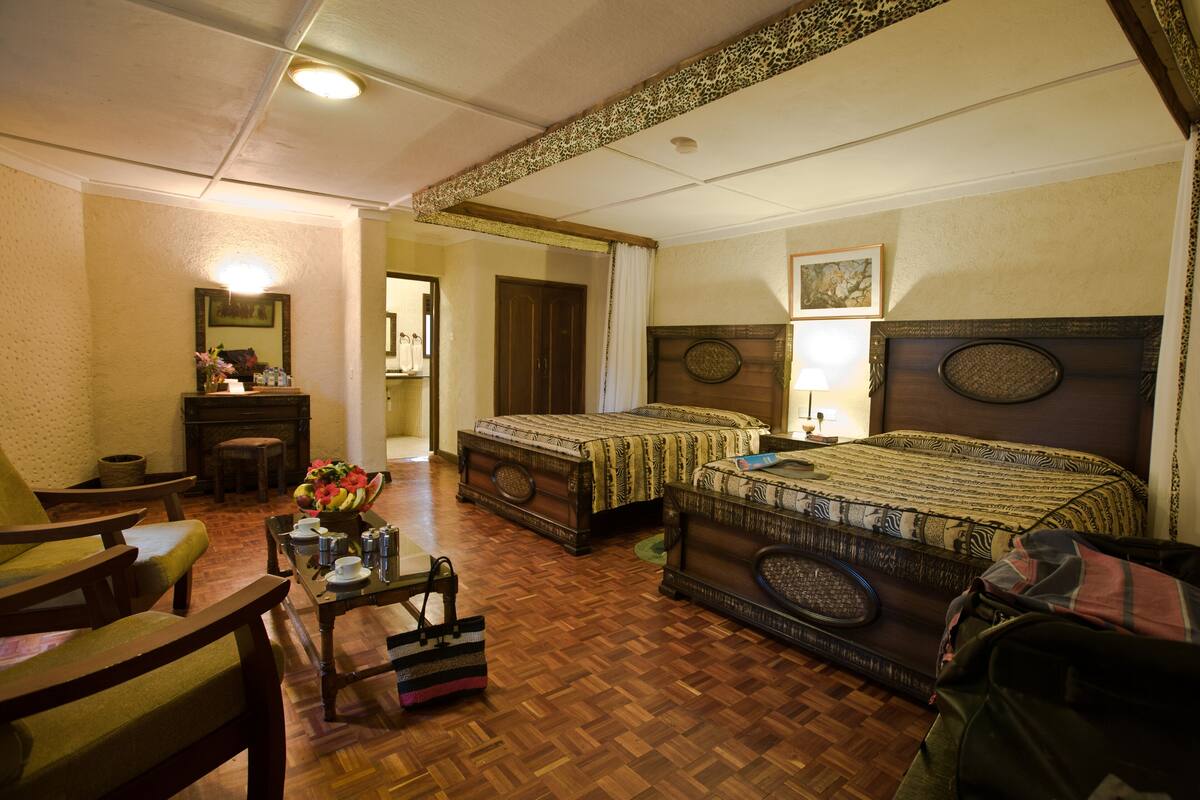Une chambre d’hôtel avec deux lits, un coin salon avec une table et des chaises, un miroir et une cheminée.