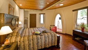 A bedroom with a wooden ceiling, a bed with patterned bedding, a nightstand with a lamp, a dresser, and a window with a view of the outdoors. - Masai Mara Sopa Lodge (Maasai Mara)