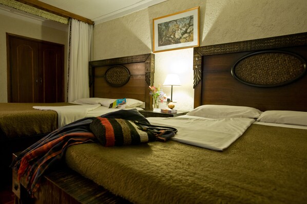 Habitación de hotel con dos camas, un cabecero de madera, un cuadro en la pared y una mesita de noche con una lámpara y flores.