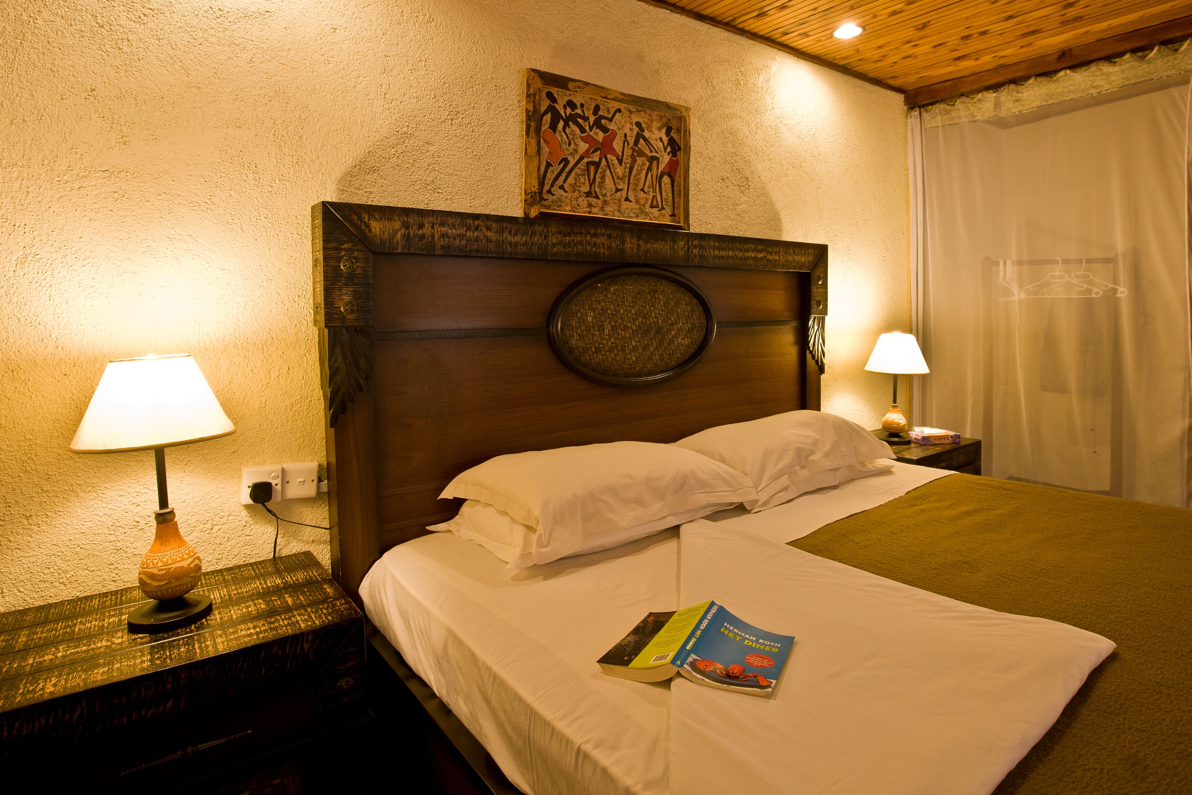 A neatly made bed with white linens and pillows, a book on the bed, and two bedside lamps on wooden nightstands.
