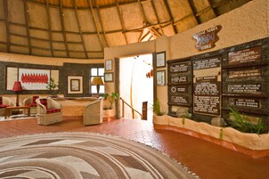 Un área de recepción con muebles de mimbre, una alfombra grande y carteles informativos sobre las normas del alojamiento.