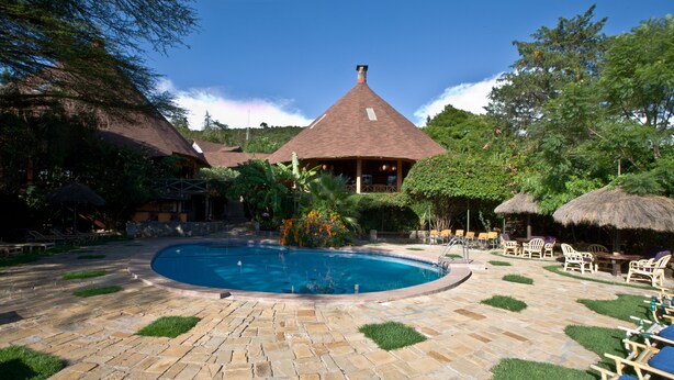 A pool area with a stone patio, lounge chairs, and a building with a conical roof. - Masai Mara Sopa Lodge (Maasai Mara)