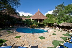 Un área de piscina con un patio de piedra, sillones de descanso y un edificio con techo cónico.