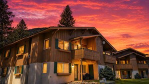 A multi-story wooden building with balconies, large windows, and a view of the surrounding landscape.