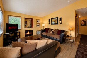 Een woonkamer met een open haard, een televisie waarop 'NETFLIX' wordt getoond, en een bank.
