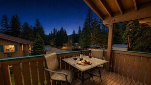 A wooden deck with a table and chairs, a bottle of wine, and a plate of cheese and grapes.