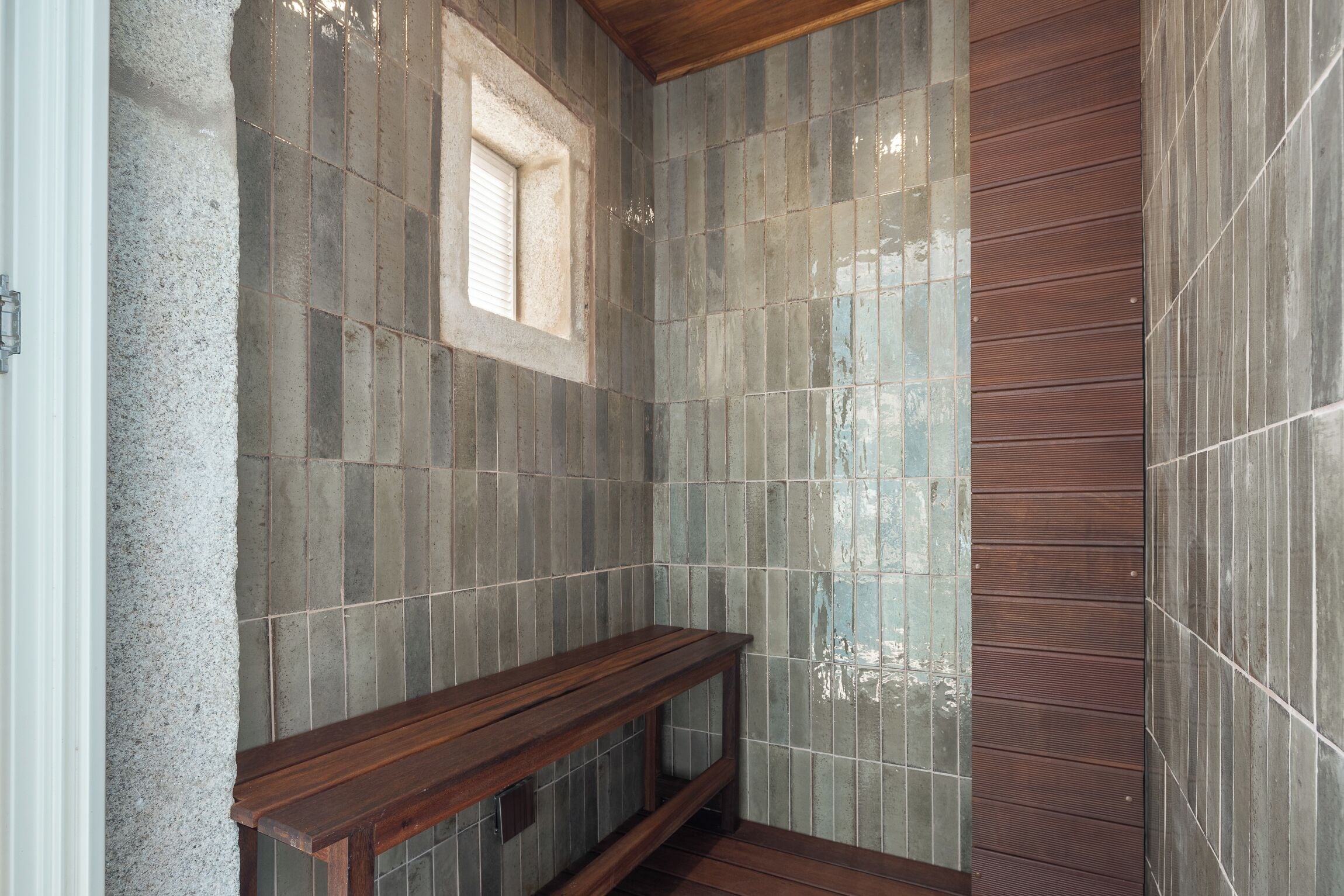 Une salle de bain avec un banc en bois, des murs carrelés et une fenêtre.