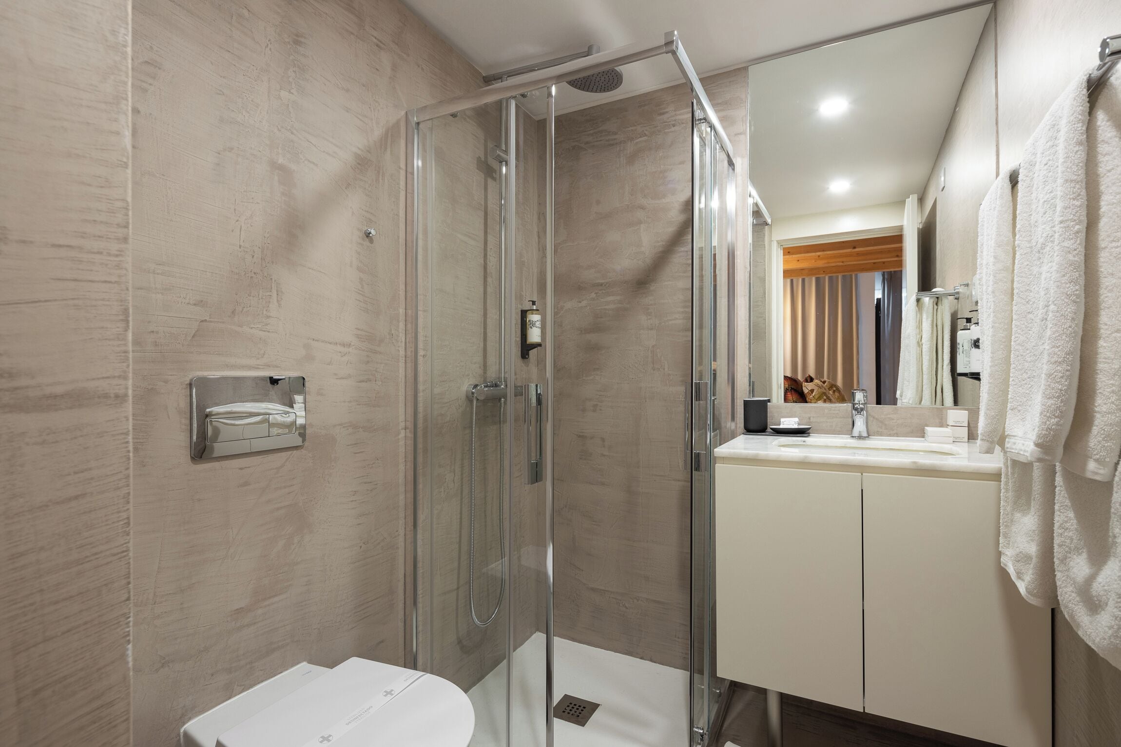 Un baño moderno con ducha acristalada, lavamanos blanco y espejo con toallero.