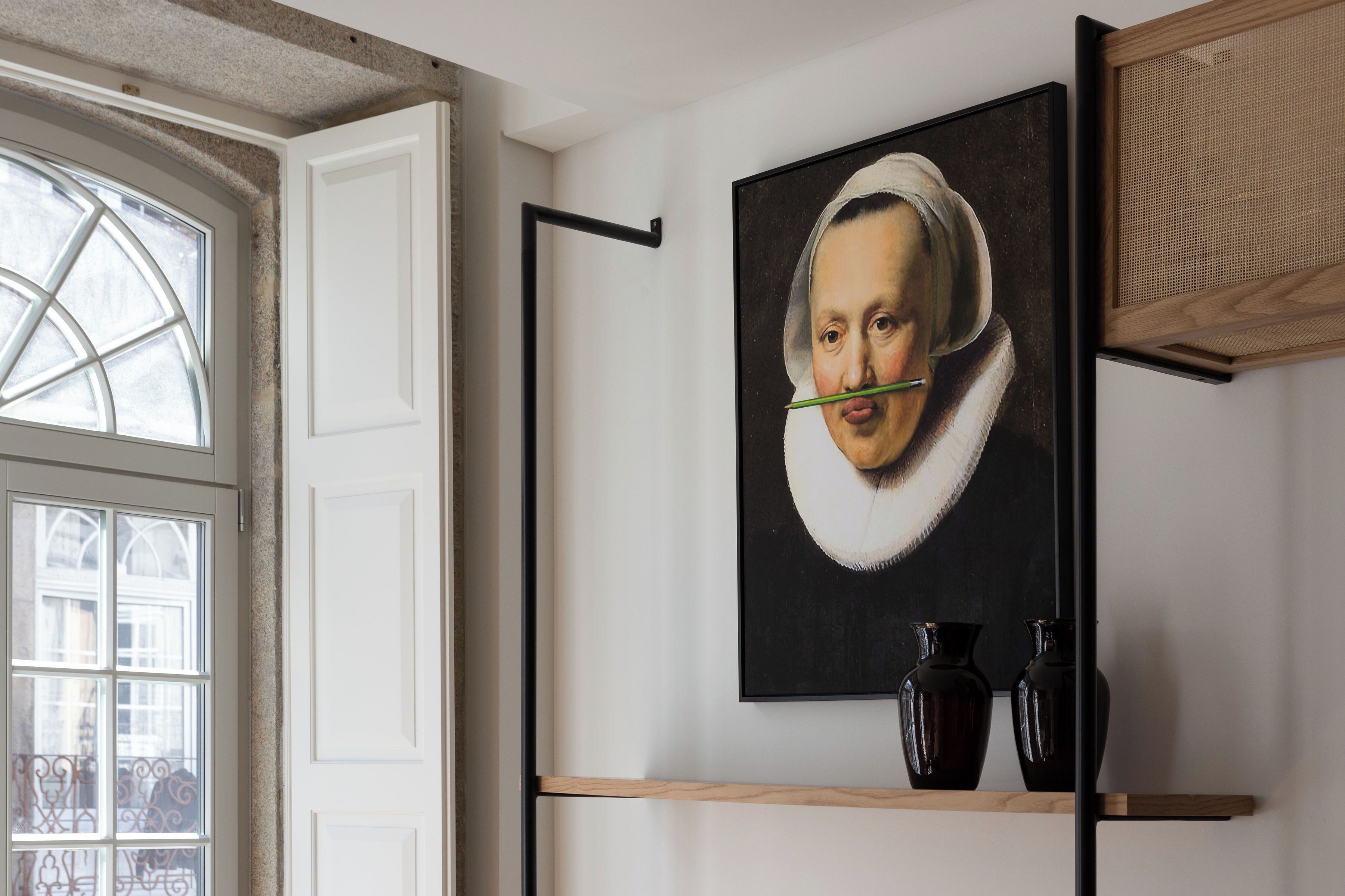 Ein Zimmer mit einem großen Fenster, einem Gemälde an der Wand und zwei dunklen Vasen auf einem Regal.