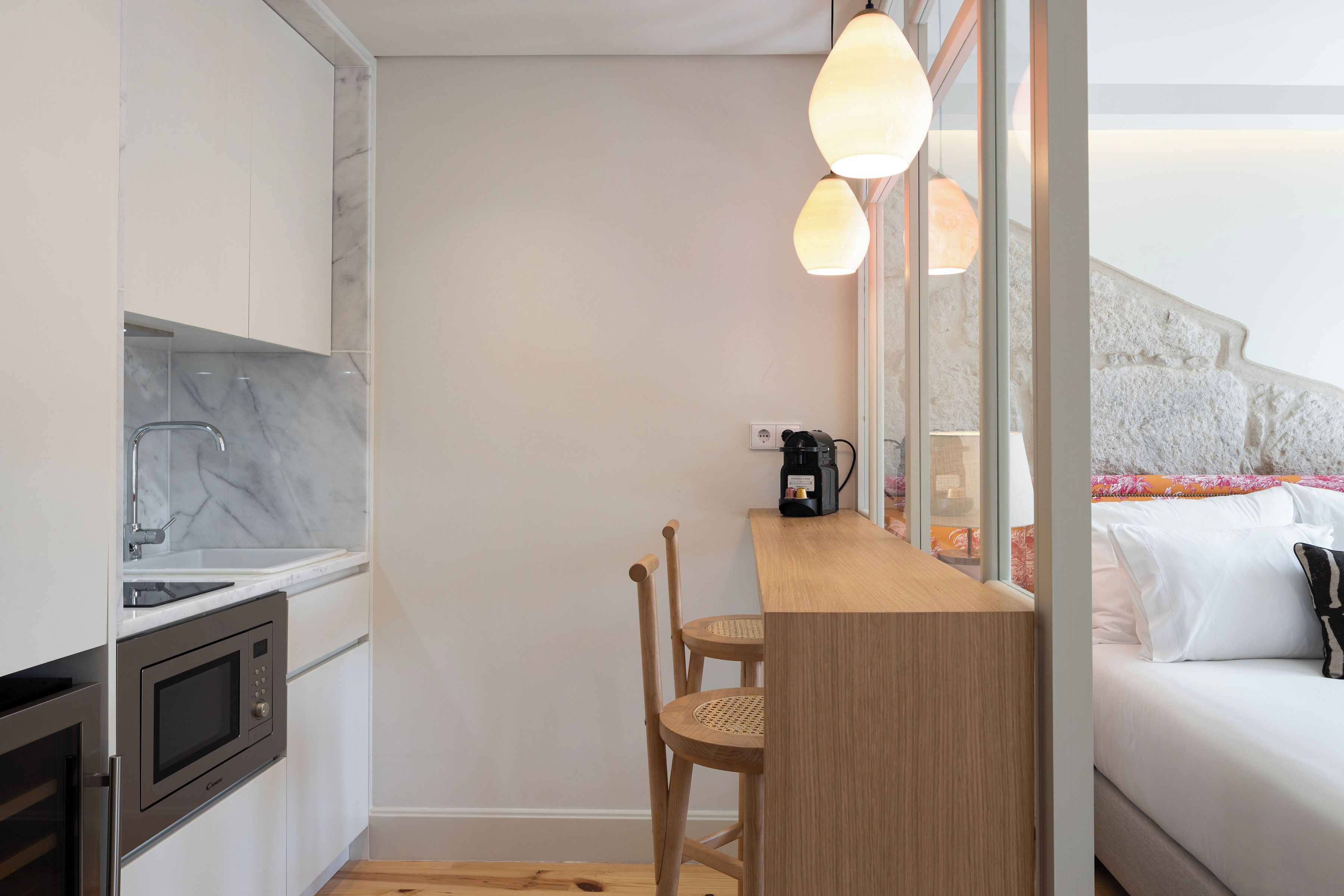 Cocina compacta con microondas integrado, un lavamanos y una barra de madera con dos sillas.