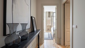 A hallway with a wooden floor, a black console table with vases, and a framed picture. There is a door leading to another room. - Líbere Porto Laranjais (Porto)