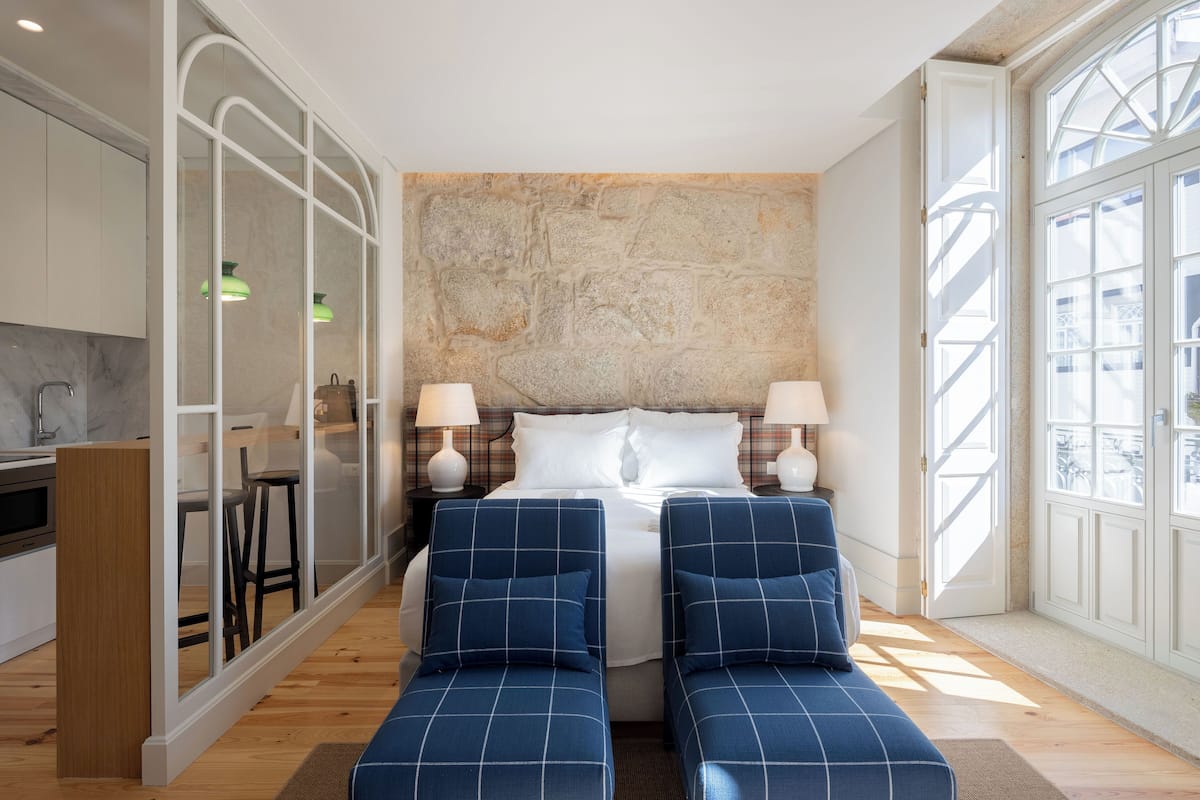 A modern hotel room with a large bed, two bedside tables, a built-in desk, and a view through a large window.