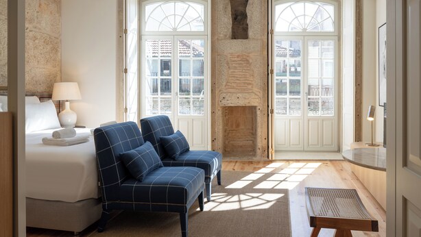 A hotel room with a bed, a blue sofa, a small table, and a fireplace. - Líbere Porto Laranjais (Porto)