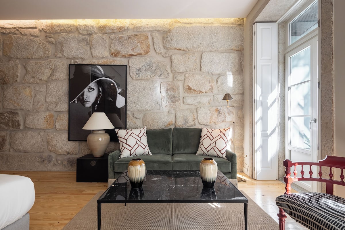 A living room with a stone wall, a green sofa, two vases on a coffee table, and a red chair.