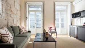 A living room with a stone wall, a green sofa, a coffee table, and a cabinet with wine glasses. - Líbere Porto Laranjais (Porto)